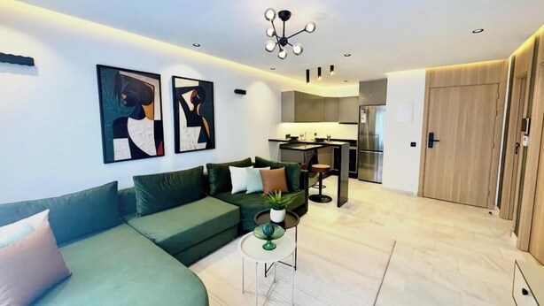 Un salon moderne avec un canapé vert, un coin repas et une cuisine en arrière-plan.