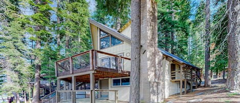 A multi-story cabin with a balcony, surrounded by trees.