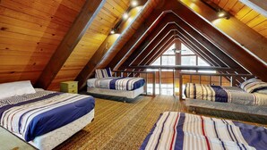 Ein gemütliches Schlafzimmer unter dem Dach mit Holzbalken, zwei Betten, einem kleinen Nachttisch und einem großen Fenster.
