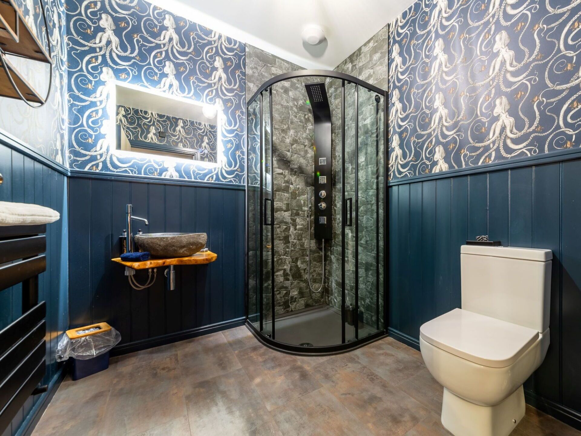 Un baño con cabina de ducha de vidrio, inodoro, lavamanos con lavabo de piedra y un perchero para toallas.