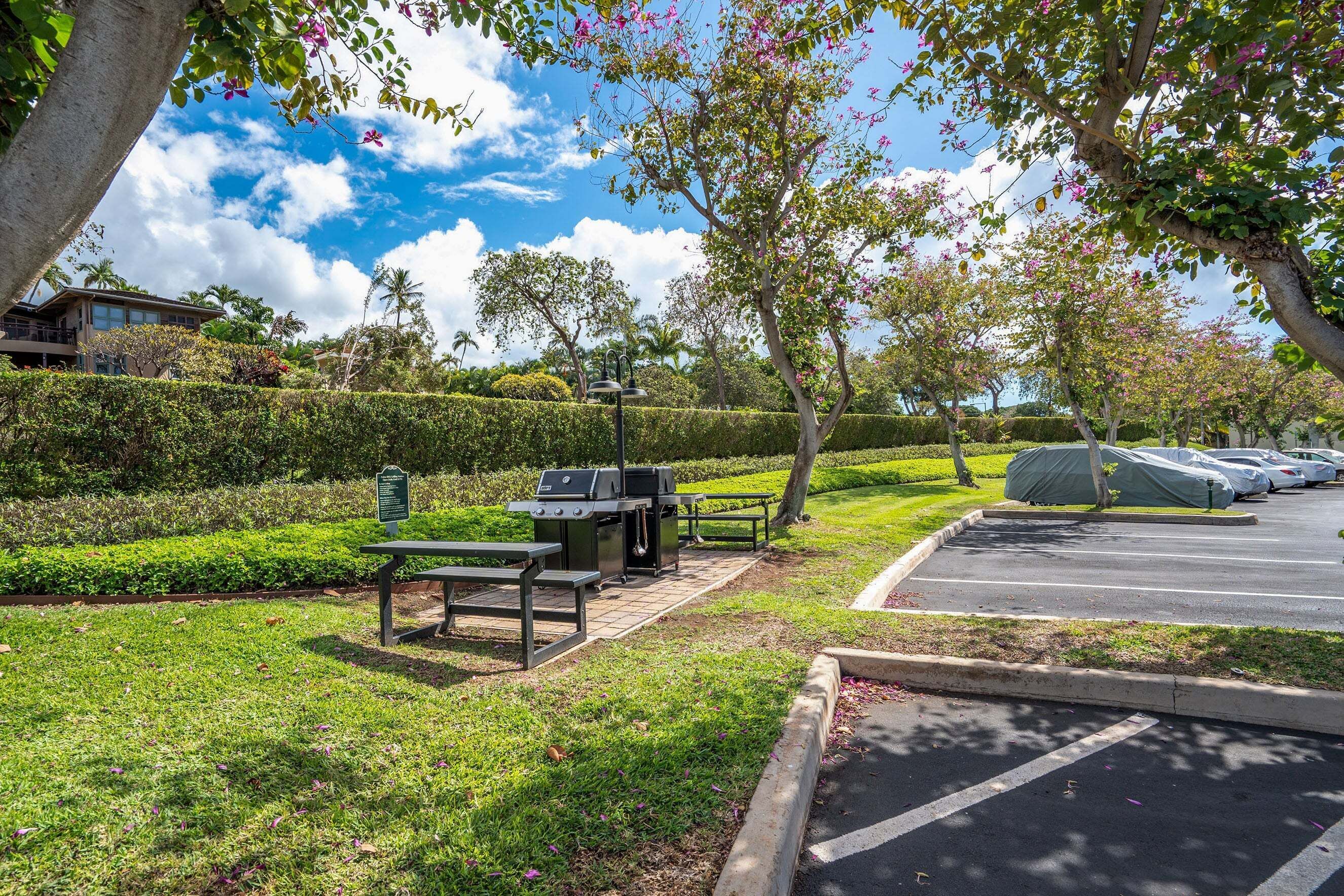 A parking lot with a barbecue grill and picnic tables.