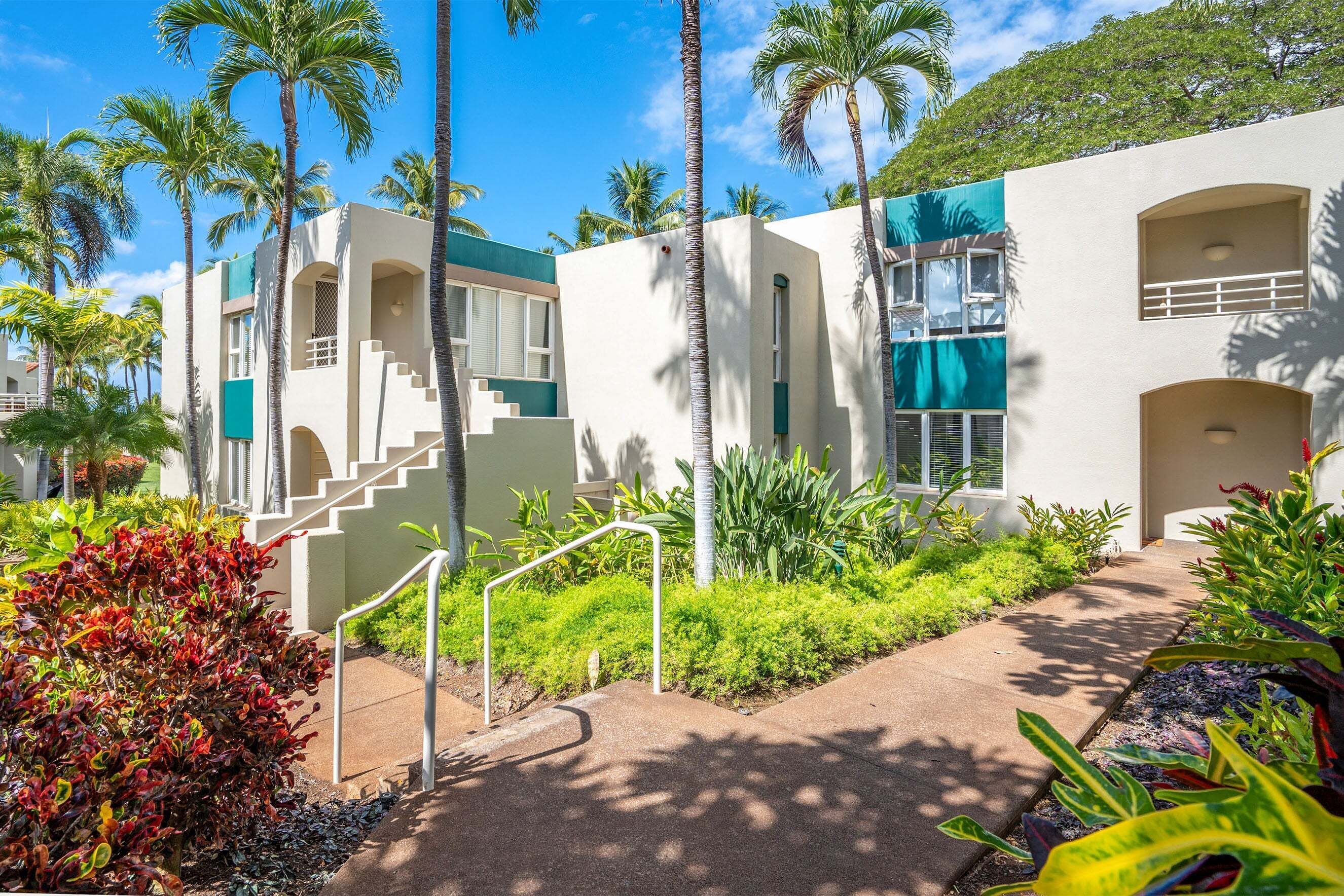 A modern building with a staircase, palm trees, and a well-maintained garden.
