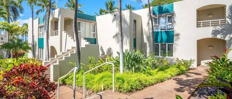 A modern building with a staircase, palm trees, and a well-maintained garden.