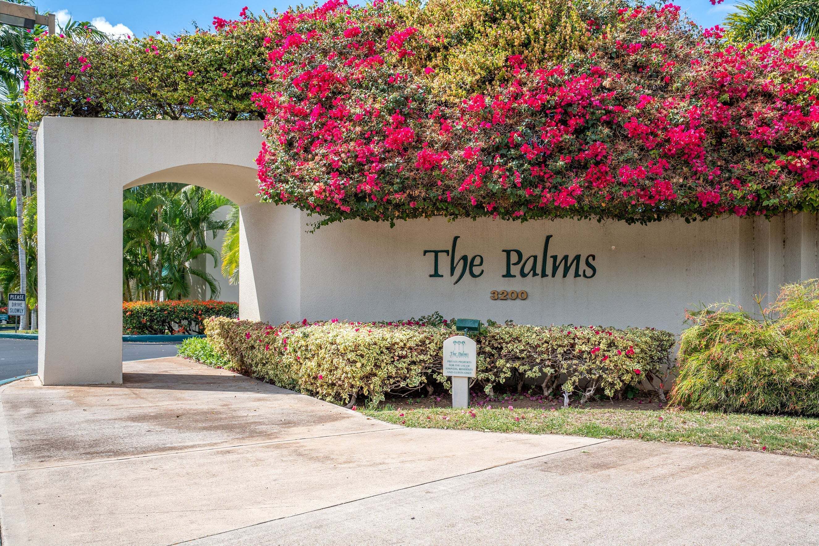 A building entrance with a sign reading 'The Palms 3200' and a lush, flowering wall.