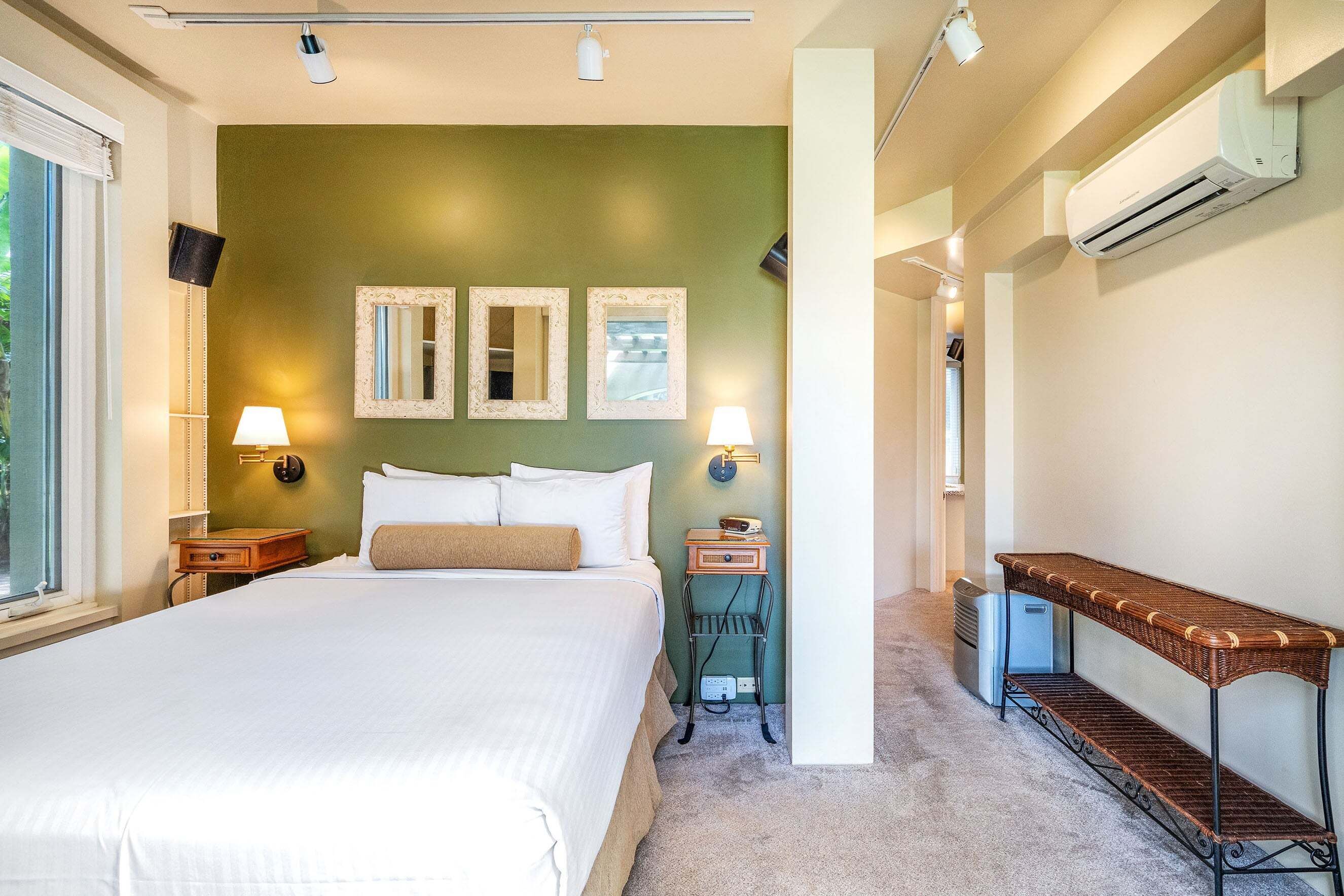 Une chambre à coucher comprenant un lit, des lampes de chevet, une table de chevet, un miroir et un appareil de climatisation.