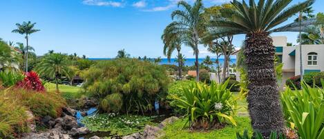 A tropical garden with a pond, palm trees, and a view of the ocean.