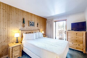 A hotel room with a wooden paneled wall, a bed with white bedding, a wooden dresser, a television, and a sliding glass door to the outside. - Find your perfect getaway to Lake Tahoe and Heavenly (South Lake Tahoe)