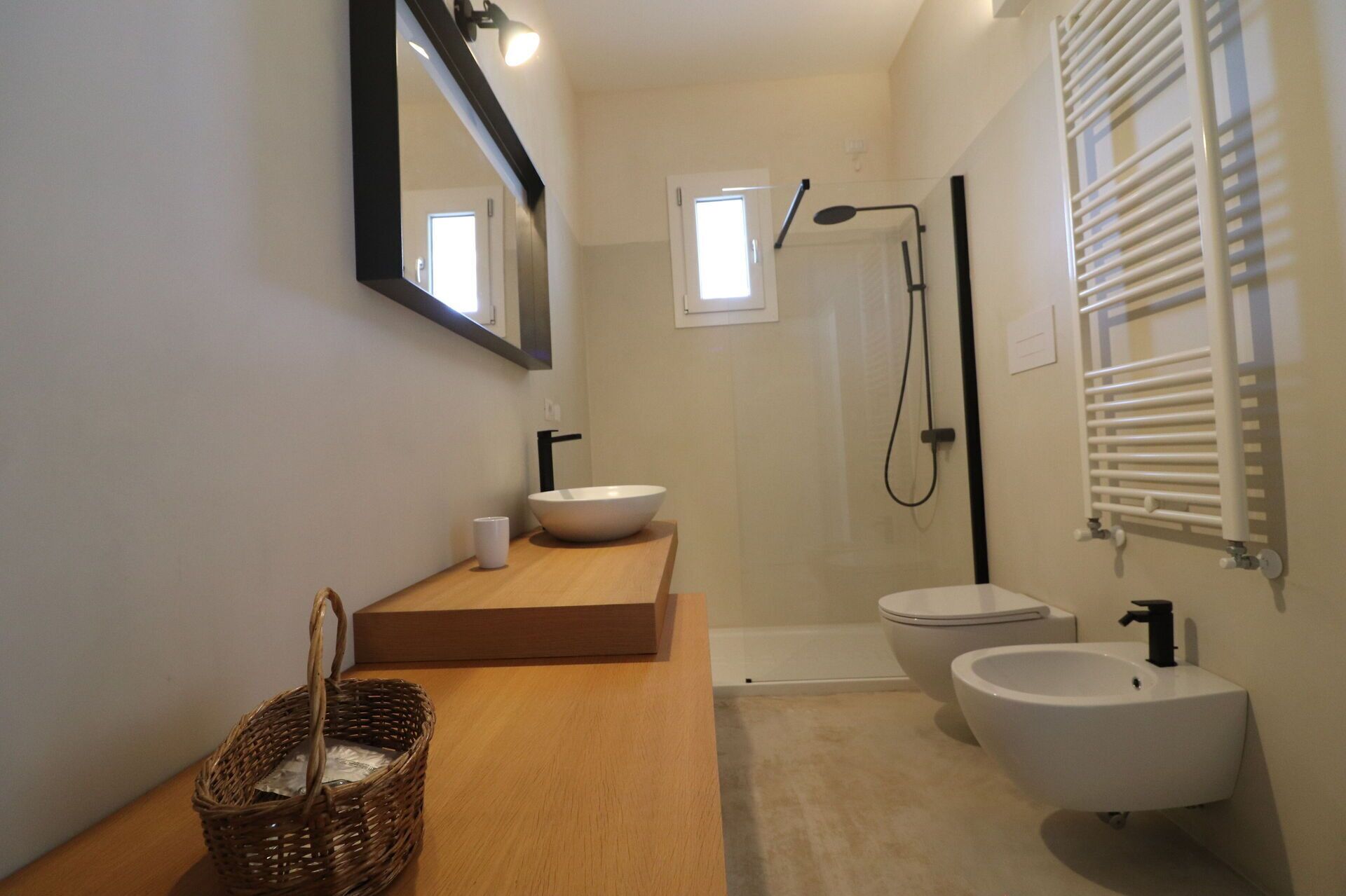 A modern bathroom with a wooden vanity, two sinks, a shower, and a towel rack.