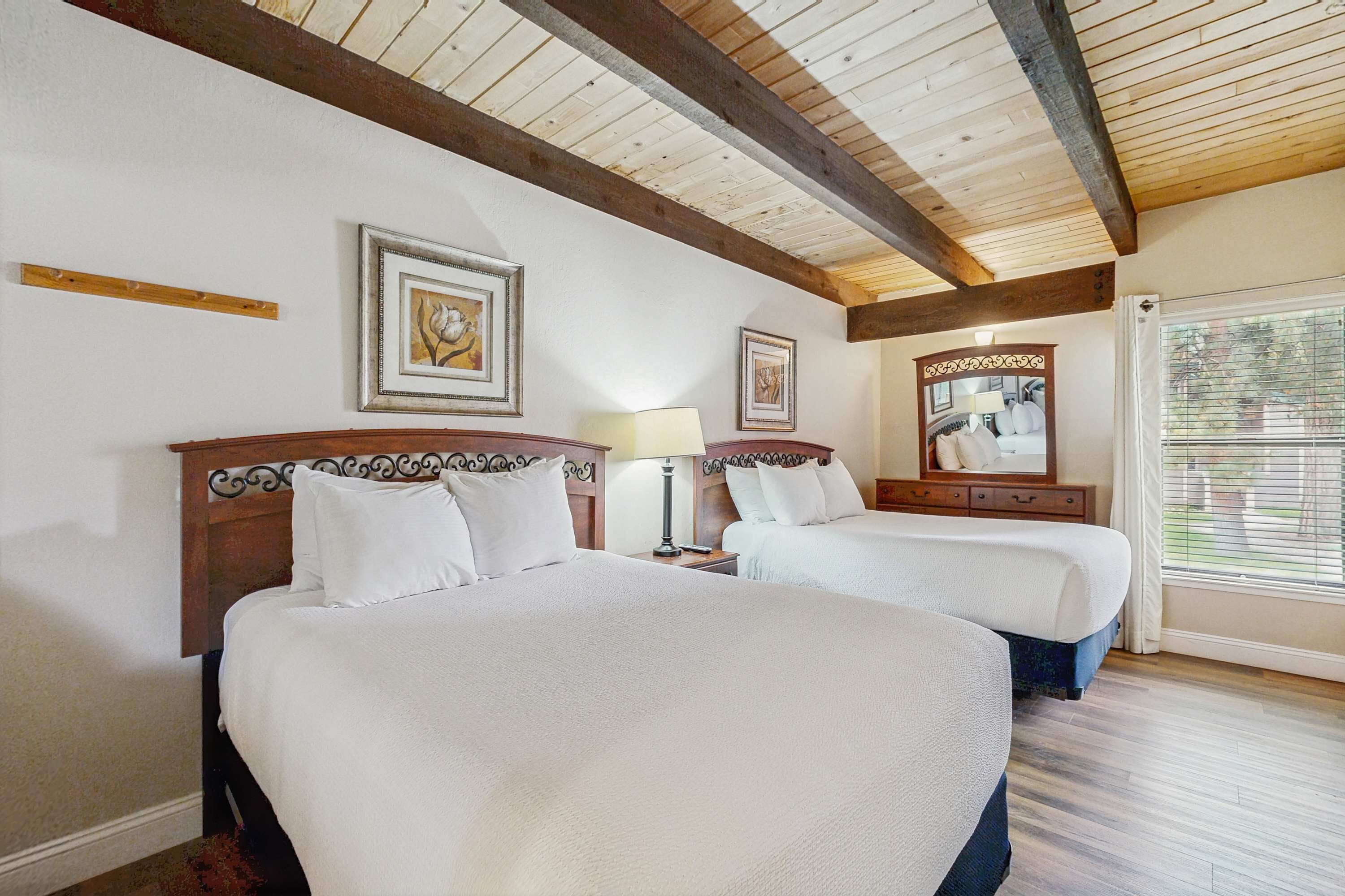 Ein Hotelzimmer mit zwei Betten, Holzbalken an der Decke, gerahmten Kunstwerken an den Wänden und einem Fenster mit Vorhängen.
