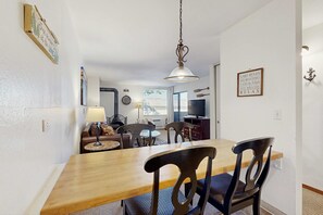 A dining area with a wooden table, black chairs, a hanging light fixture, and a wall-mounted sign. - Comfortable condo with pool, sauna, and hot tub access (South Lake Tahoe)