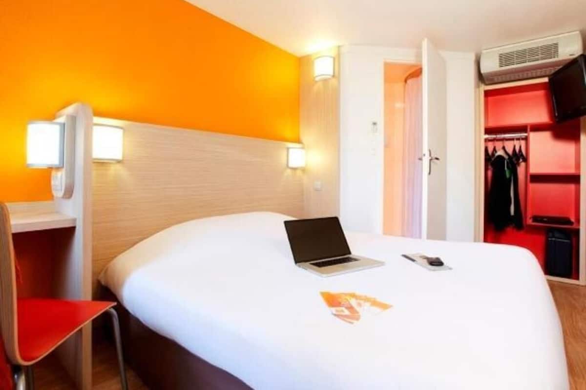 A hotel room with a bed, a laptop, a chair, a desk, and a wardrobe.