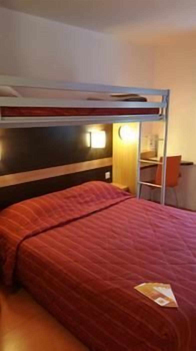 Una cama tipo litera con colchón rojo, un escritorio con silla y una lámpara fijada a la pared.