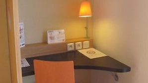 A small hotel room with a desk, chair, and a wall-mounted lamp. - B&B Hotel Bayeux (Bayeux)