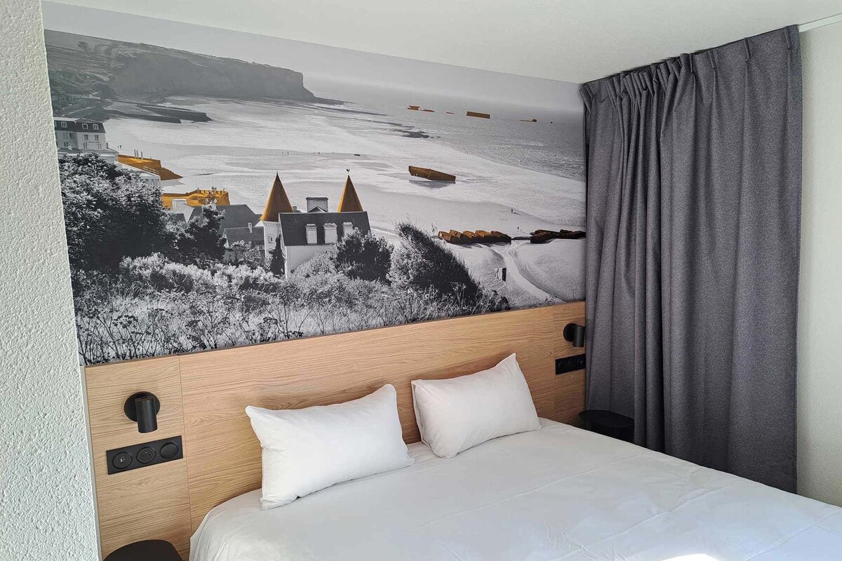 A hotel room with a large bed, a headboard with a mural, and a grey curtain.