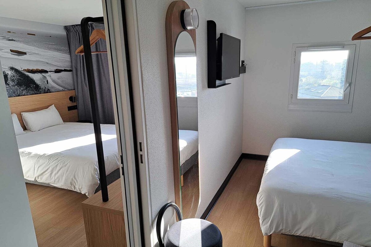 A bedroom with two beds, a television mounted on the wall, and a window providing a view of the outside.