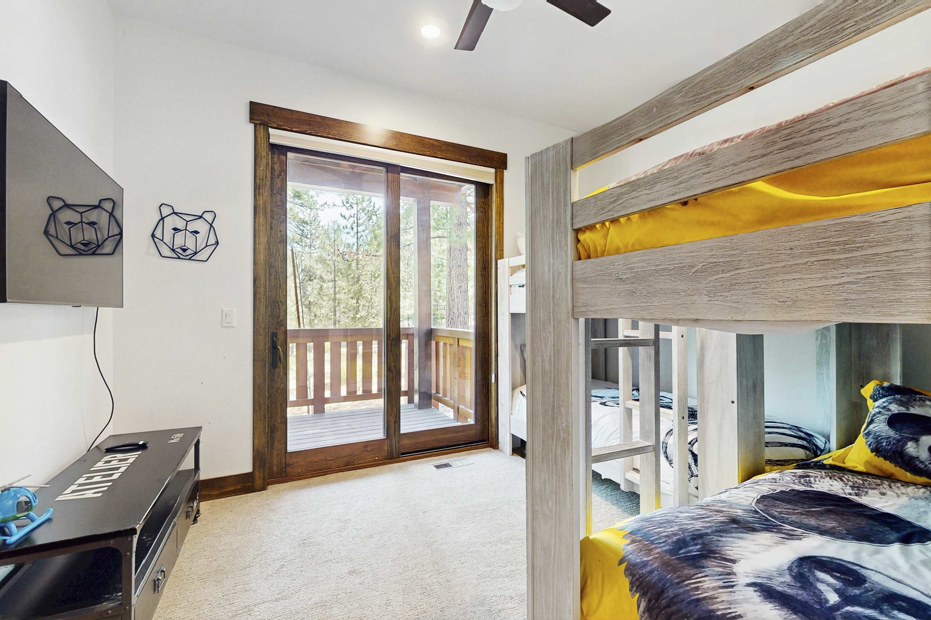 Un dormitorio con una cama litera, un escritorio con computadora, una puerta corrediza al balcón y dos cuadros con temática de osos.