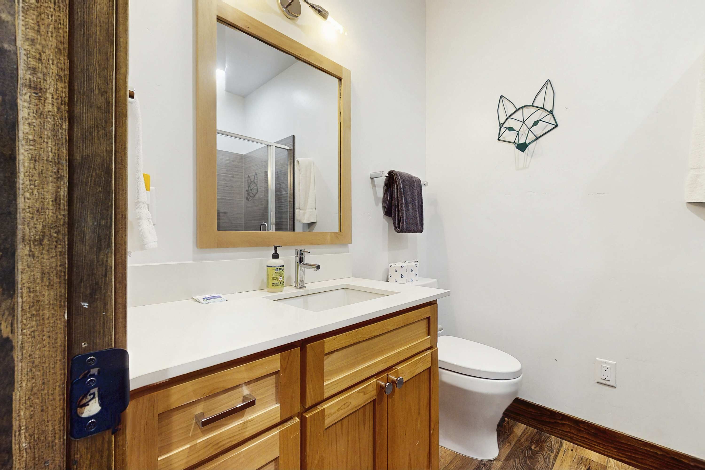 Une salle de bain avec un meuble-lavabo en bois, un lavabo blanc, un miroir, des toilettes et un motif géométrique sur le mur.