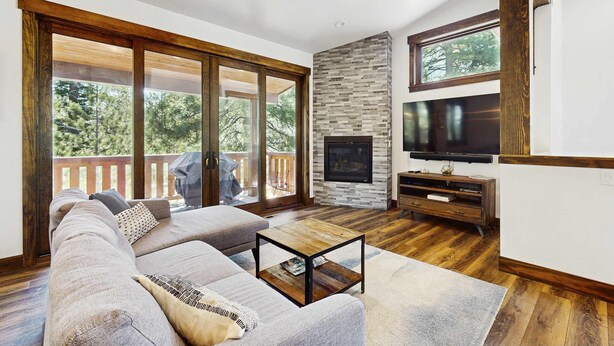 Ein modernes Wohnzimmer mit einer großen Eckcouch, einem Couchtisch, einem Kamin, einem Fernseher und einem Balkon mit Holzterrasse.