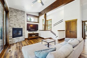 A modern living room with a fireplace, a large sofa, a television, and a staircase. - Cozy & contemporary townhome with two decks - close to town & outdoor fun (Truckee)