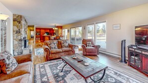 A spacious living area with a stone accent wall, a fireplace, a large coffee table, and a television. - Cozy Retreat - On Golf Course, Near Skiing, Hot Tub (South Lake Tahoe)