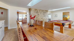 A spacious room with a wooden pool table, a dining table with chairs, a stone accent wall, and a skylight. - Cozy Retreat - On Golf Course, Near Skiing, Hot Tub (South Lake Tahoe)