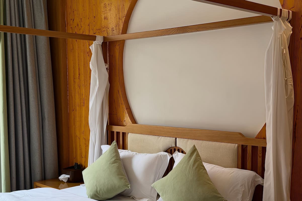 Una cama con cabecera de madera, ropa de cama blanca y almohadas verdes.