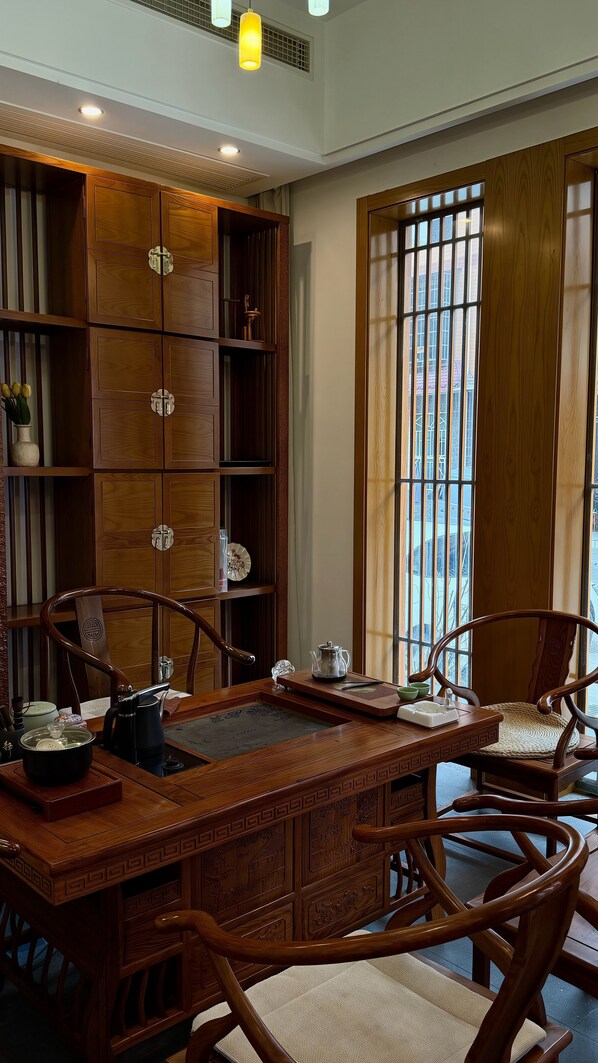 A traditional wooden desk with chairs, a window with a view, and a shelf with decorative items.