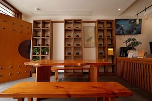 A reception area with a wooden reception desk, shelves with teapots, a framed artwork, and a television screen.