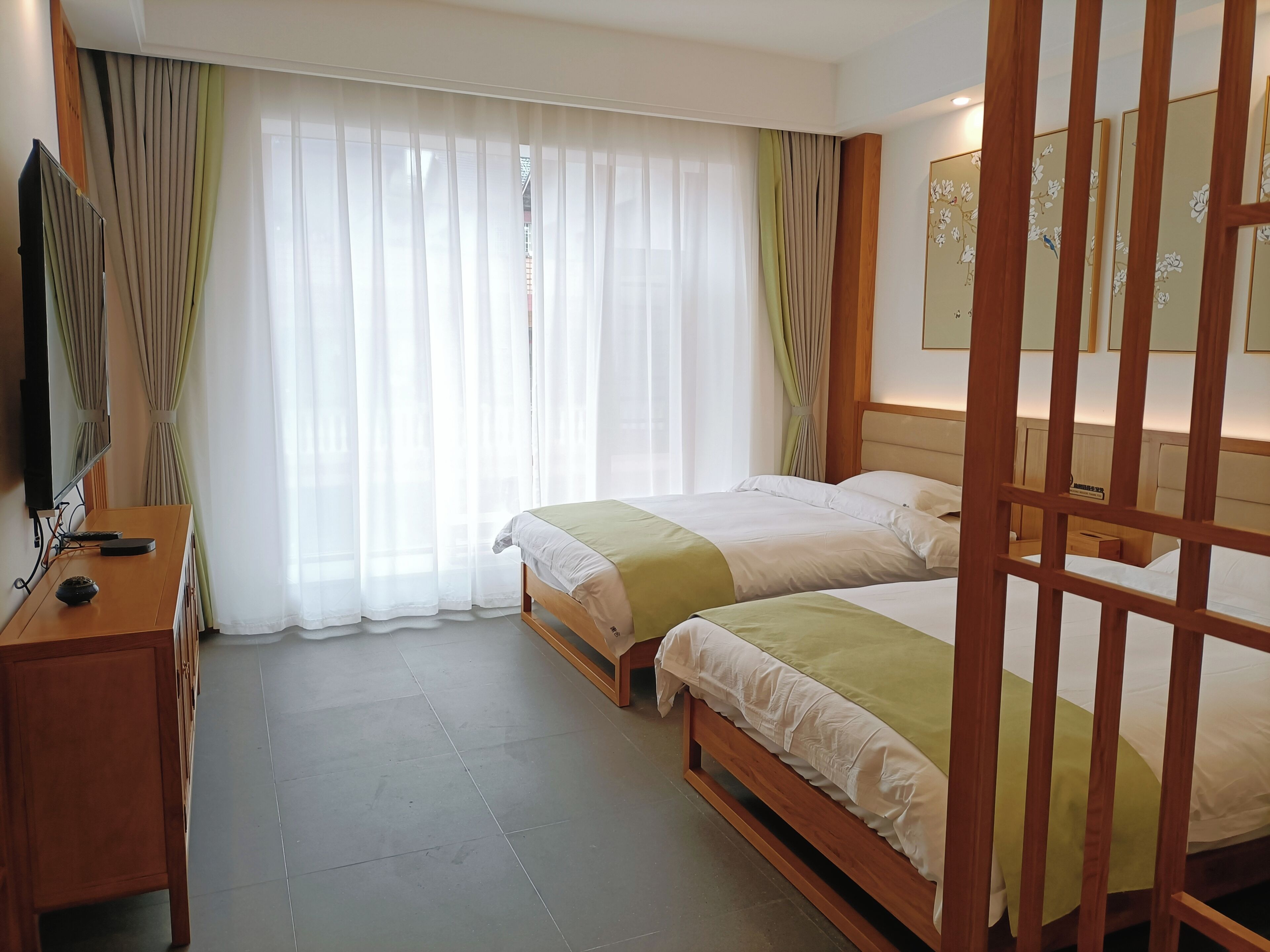 Habitación de hotel con dos camas, un escritorio de madera, televisor y un ventanal con cortinas.