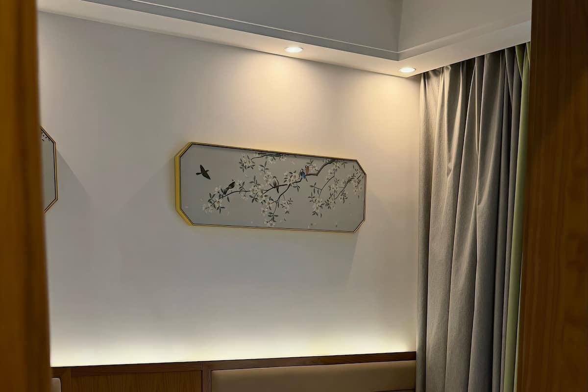 Habitación de hotel con dos camas, una mesita de noche con cafetera, un reloj en la pared y una ventana con cortinas.