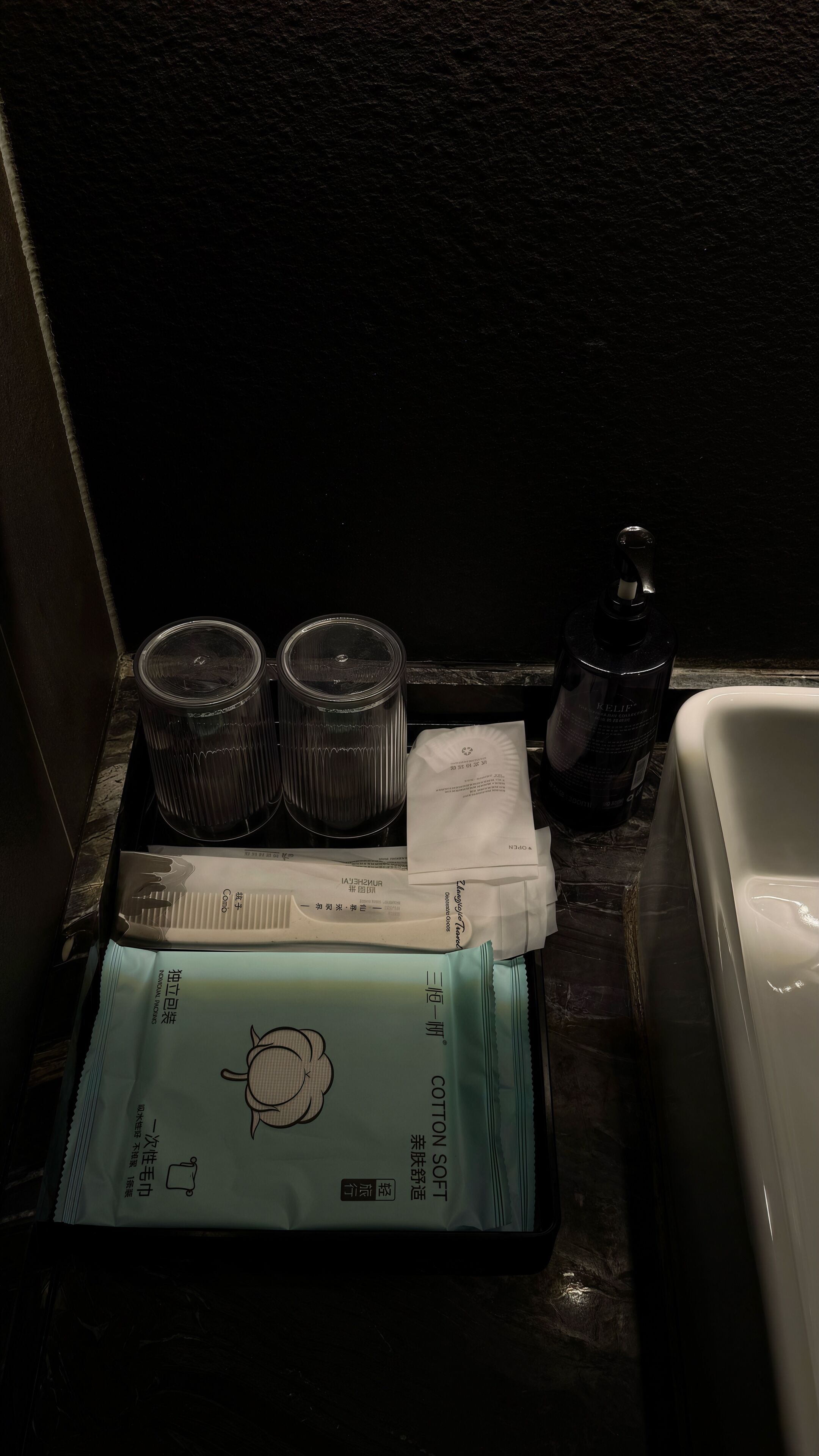 Ein Badezimmer mit einem Waschbecken, zwei Glasbehältern, einer Flasche und einer Packung Wattestäbchen.