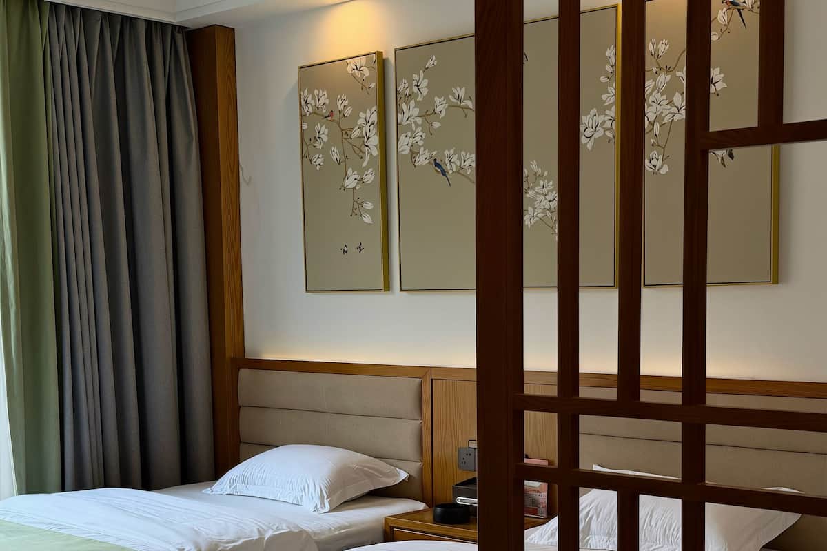 Habitación de hotel con dos camas, cabecera de madera, luz empotrada en la pared y un panel decorativo con pájaros.