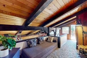 Um quarto de sótão aconchegante com teto de madeira, um sofá com almofadas, uma planta em vaso e uma escrivaninha com abajur.