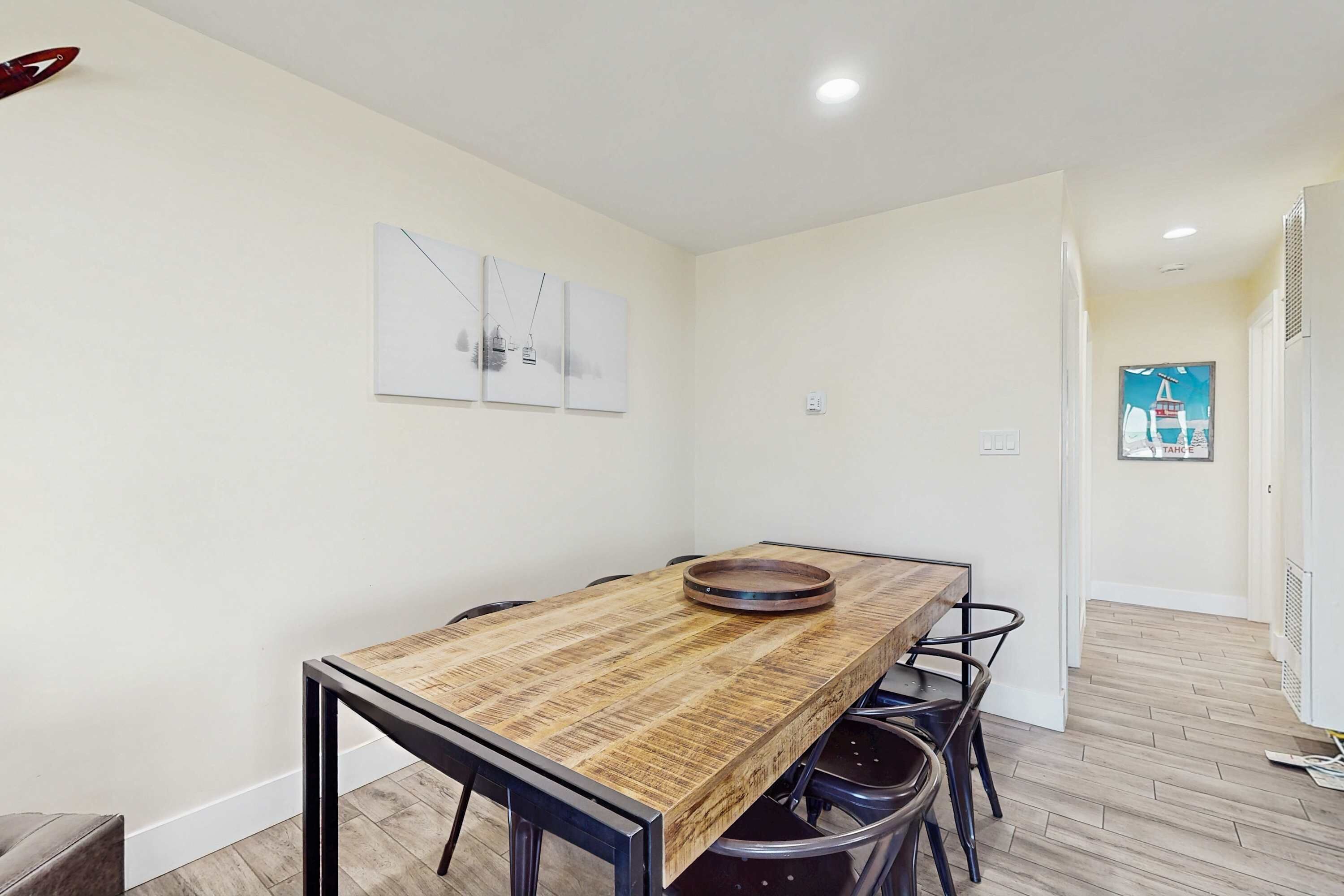 A dining area with a wooden table and chairs, a wall-mounted light fixture, and a door leading to another room.