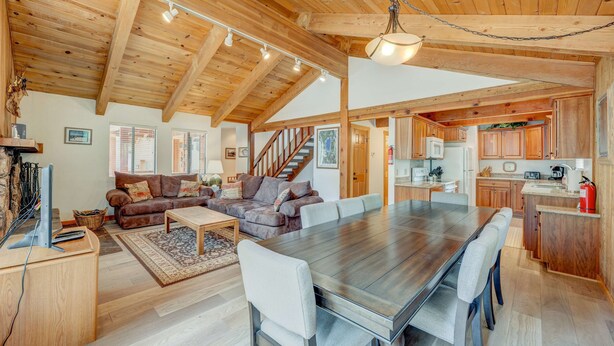A spacious living area with a large wooden dining table, a sofa set, and a kitchen with wooden cabinets and a built-in stove.