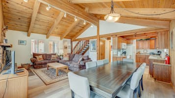 A spacious living area with a large wooden dining table, a sofa set, and a kitchen with wooden cabinets and a built-in stove.