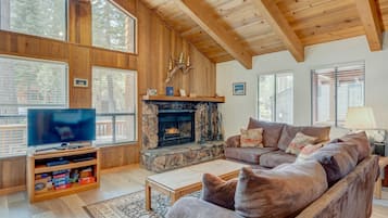 A cozy living room with a stone fireplace, wooden beams, a large TV, and a comfortable sofa.