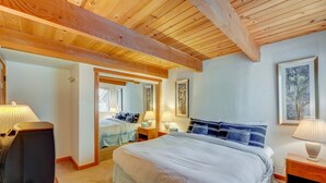 A bedroom with a large bed, wooden ceiling beams, a television, and a mirror.