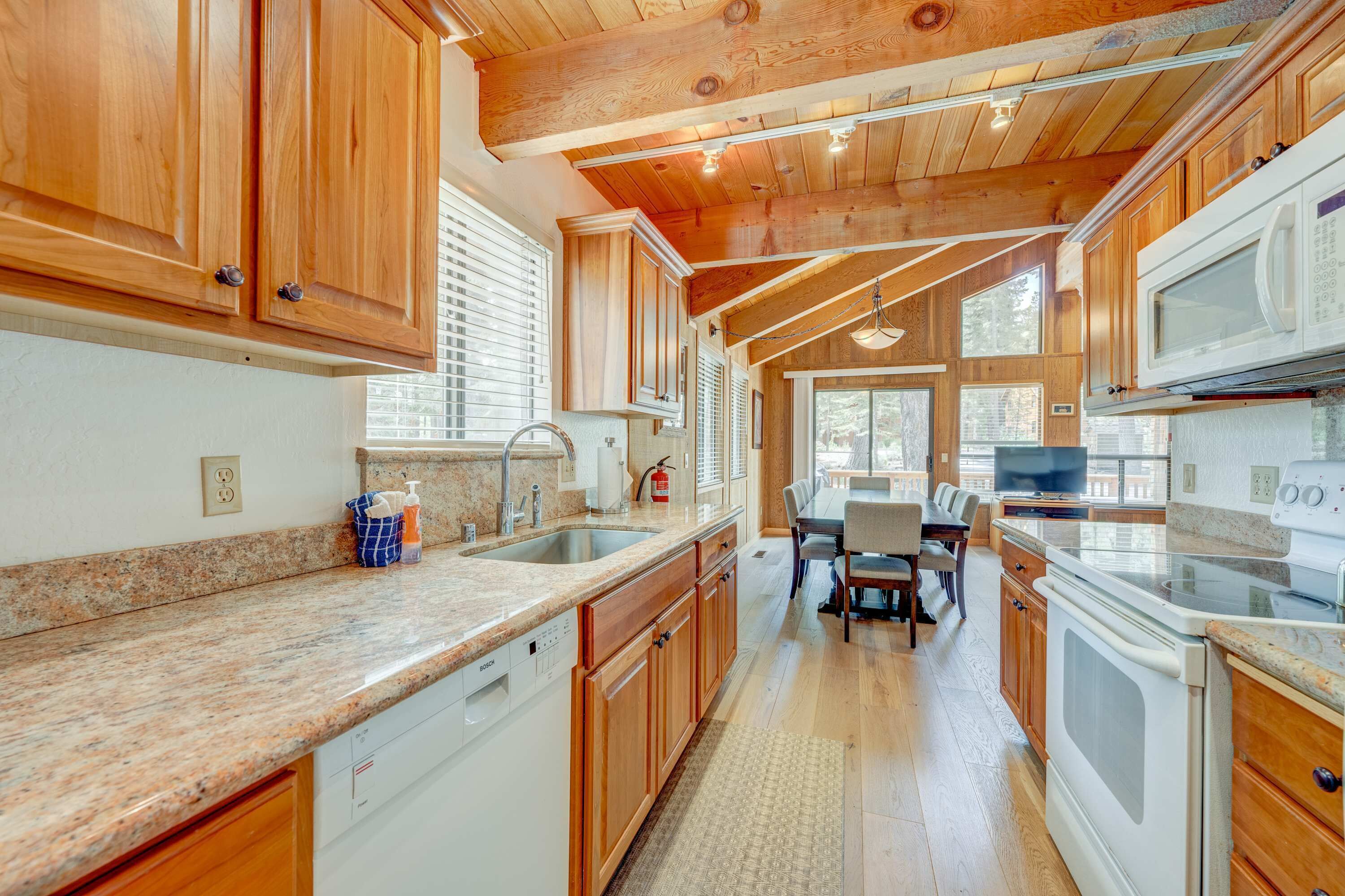 A kitchen with wooden cabinets, granite countertops, a dishwasher, a stove, and a dining area with a table and chairs.