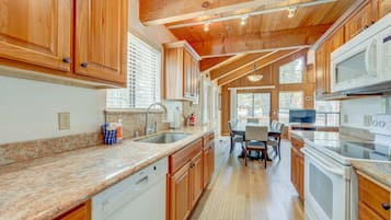 A kitchen with wooden cabinets, granite countertops, a dishwasher, a stove, and a dining area with a table and chairs.