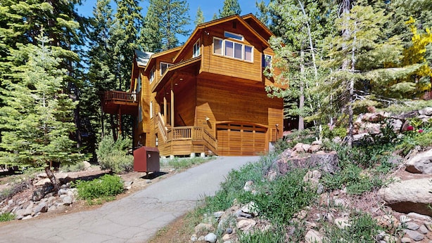 Una baita di legno con un garage, immersa tra gli alberi e un sentiero sterrato.