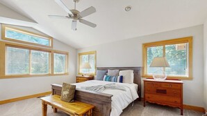 Una camera da letto con un letto, comodini in legno, una panca, una ventola a soffitto e ampie finestre.