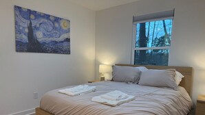 A bedroom with a bed, a painting, a window, and a nightstand.