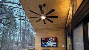 A wooden deck with outdoor seating, a ceiling fan, and a TV mounted on the wall.