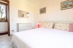 Une chambre à coucher avec un lit, une table de chevet, une lampe, un miroir et deux tableaux encadrés accrochés au mur.