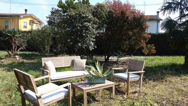 Un espace extérieur aménagé avec un banc et des chaises en bois, une petite table et une plante en pot.
