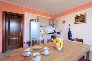 Un coin repas avec une table en bois, des chaises, un panier de fruits et une cuisine en arrière-plan.