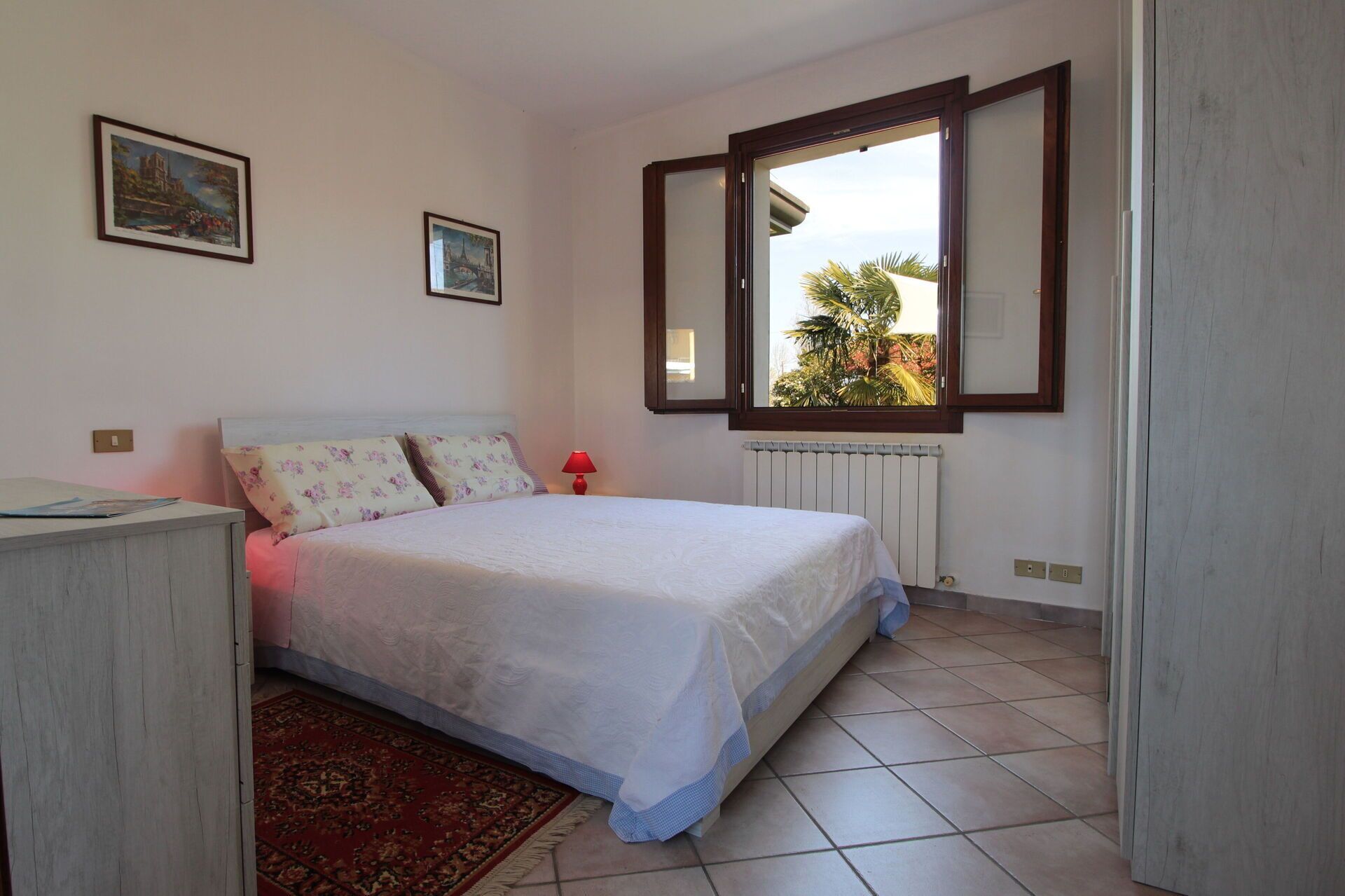 A bedroom with a bed, a radiator, a window with a view, and a desk.