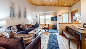 A living room with a sofa, coffee table, and a TV. There's a fireplace, a dining table with benches, and a ceiling fan. - Modern retreat with wooden touches, shared hot tub, pool, sauna, basket & tennis (Truckee)