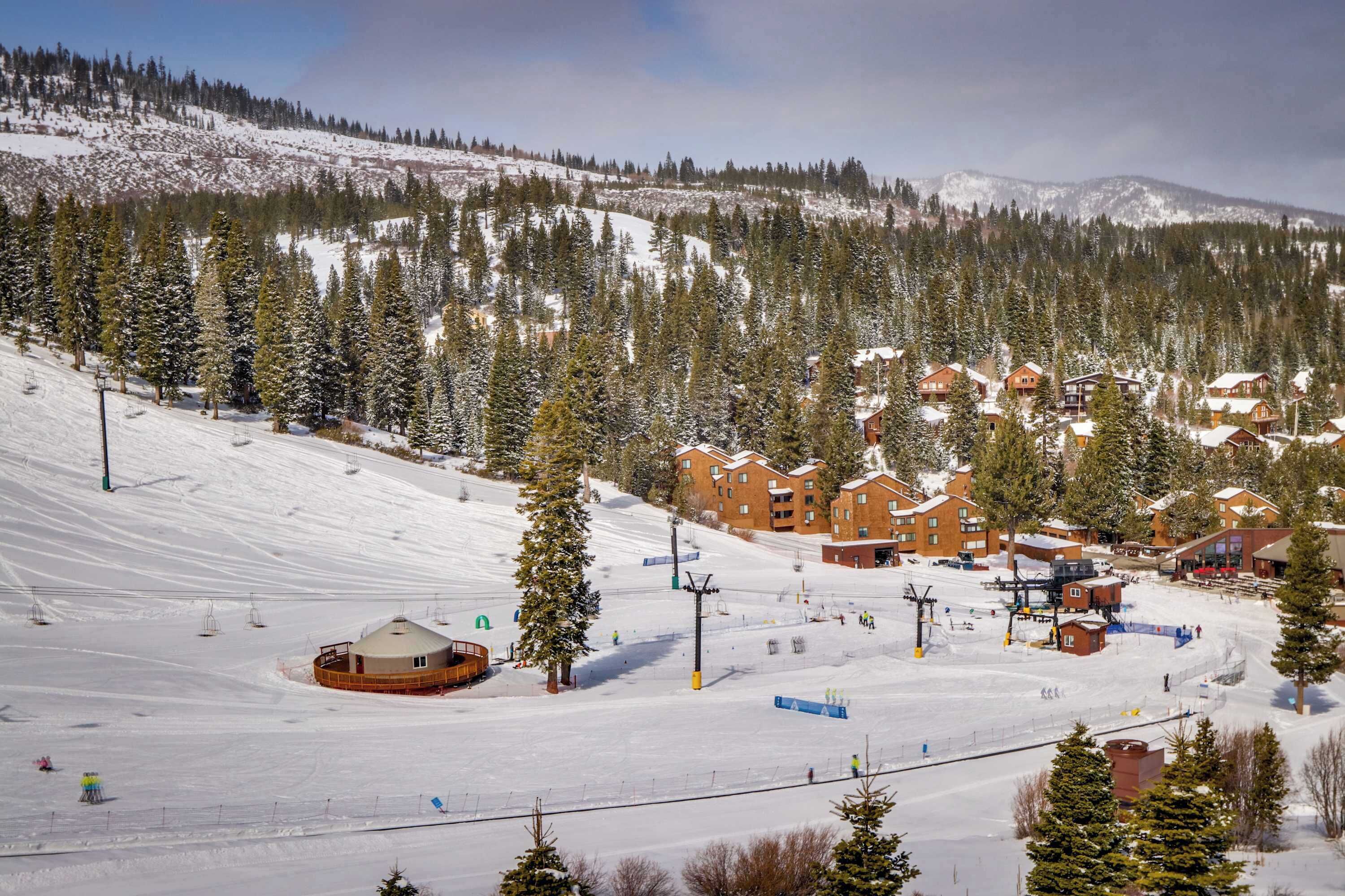 Un centro de esquí con varias cabañas, un telesilla y un paisaje cubierto de nieve.